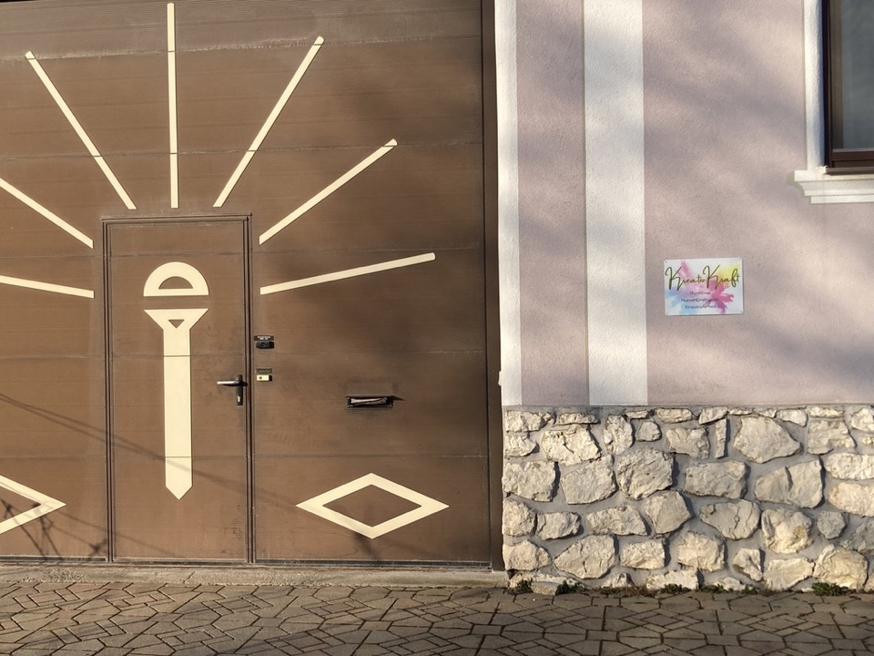 Eingang zur Praxis: braunes Tor mit Sonnenstrahlen-Motiv und KreativKraft-Schild